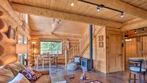 A cozy log cabin interior with a wooden staircase, a dining area, and a fireplace.