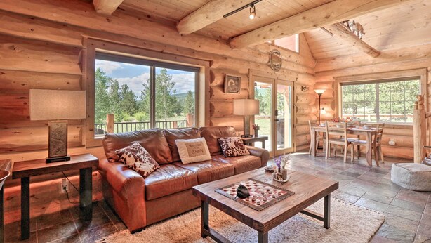 A cozy log cabin interior with a leather sofa, a wooden coffee table, and a dining area.