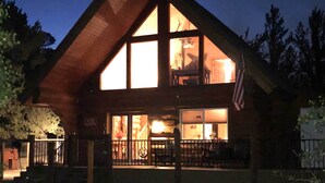 A two-story log cabin with large windows, a balcony, and an American flag.