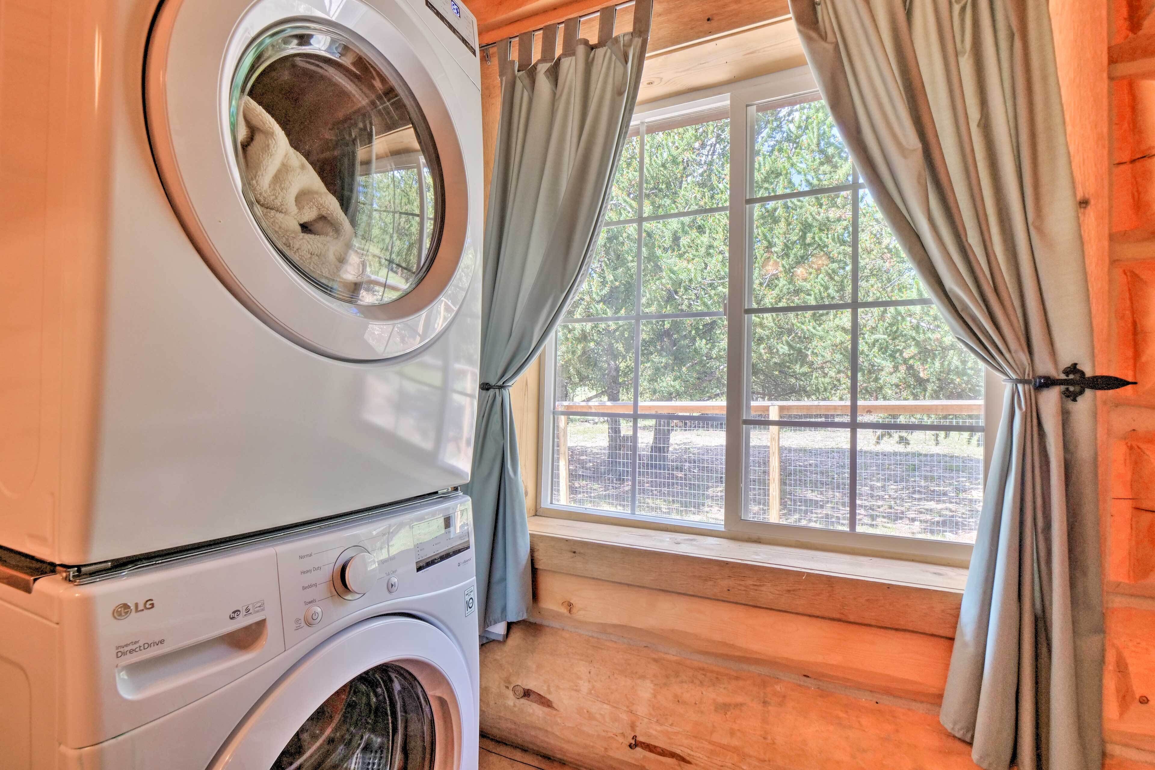 Un lavadero con lavadora y secadora, una ventana con cortinas y vistas al exterior.
