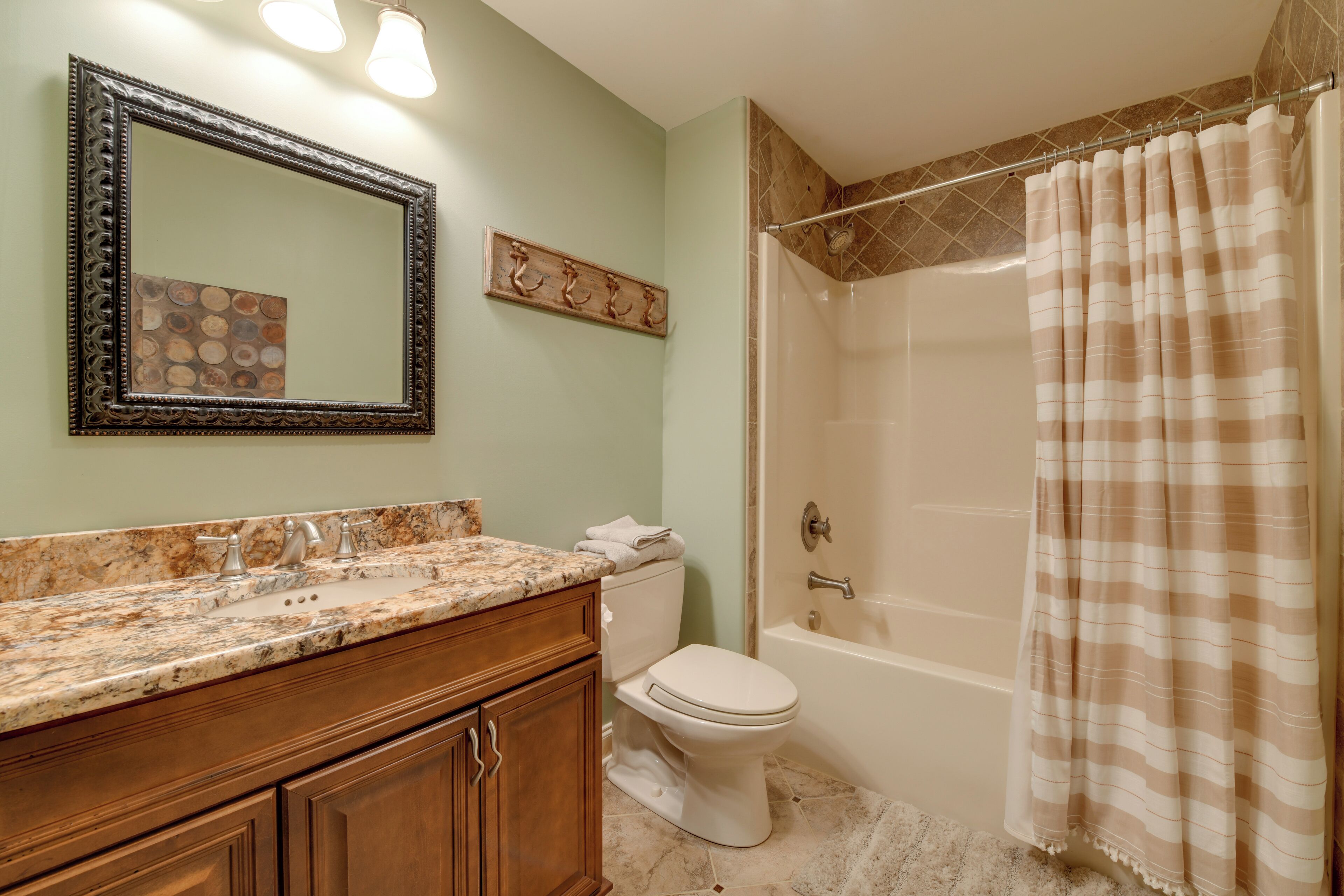 A bathroom with a marble countertop, wooden cabinets, a white toilet, a bathtub, and a shower curtain.