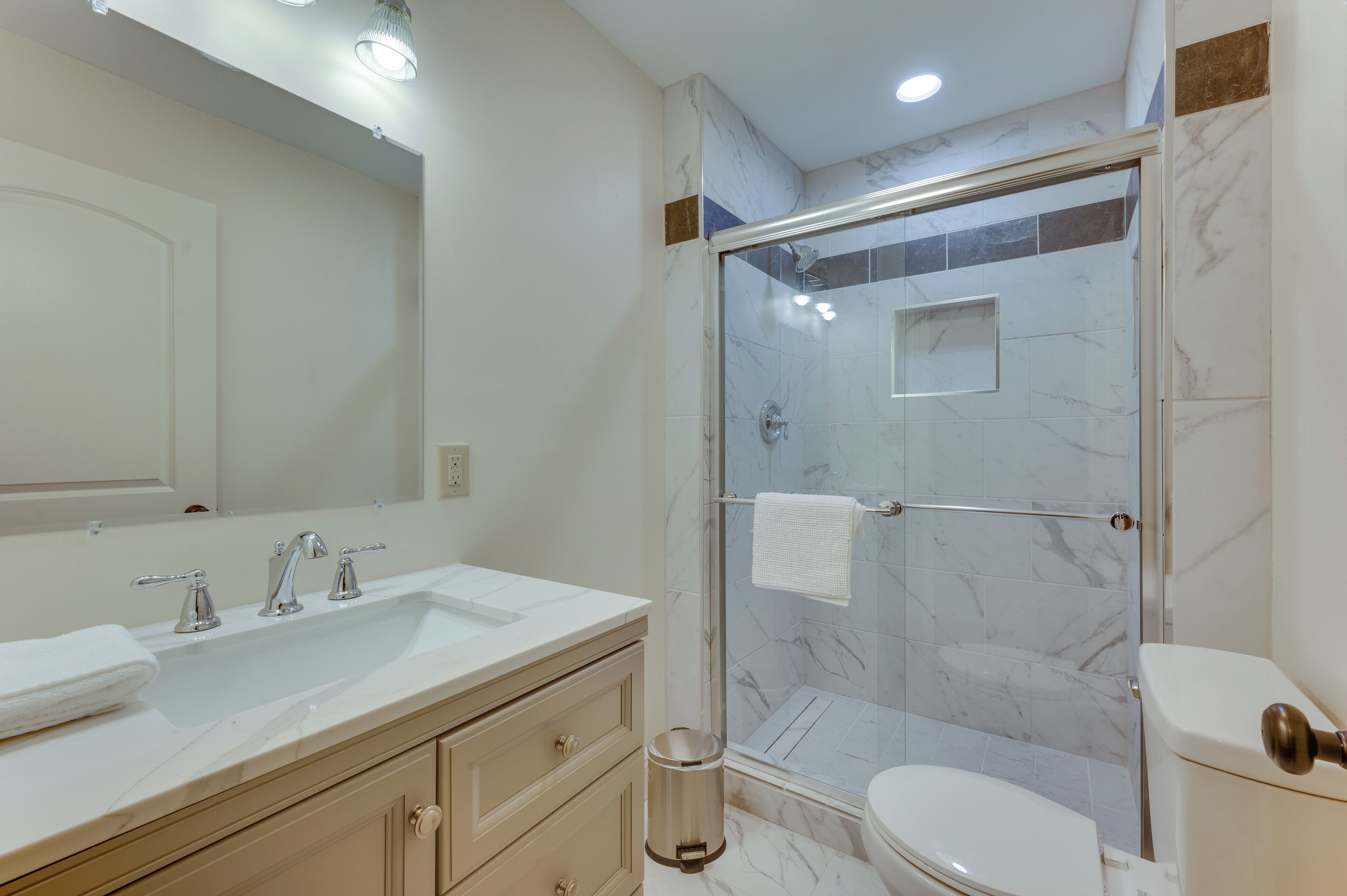 A modern bathroom with a glass-enclosed shower, a double sink vanity, and a toilet.