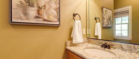 A bathroom with a granite countertop sink, a large mirror, and a framed painting of plants.