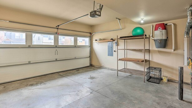 Un garage avec un sol en béton, un projecteur fixé au plafond, un chauffe-eau et un ballon d’exercice vert posé sur une étagère.