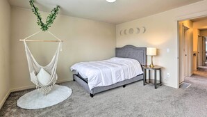 Une chambre à coucher comprenant un lit, un fauteuil suspendu, une table de chevet avec une lampe et une porte donnant sur une autre pièce.
