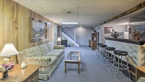 A cozy living area with a sofa, a coffee table, and a bar with stools. A staircase is visible in the background. - Cozy White Pine Home - 10 Mi to Porcupine Mtn (White Pine)