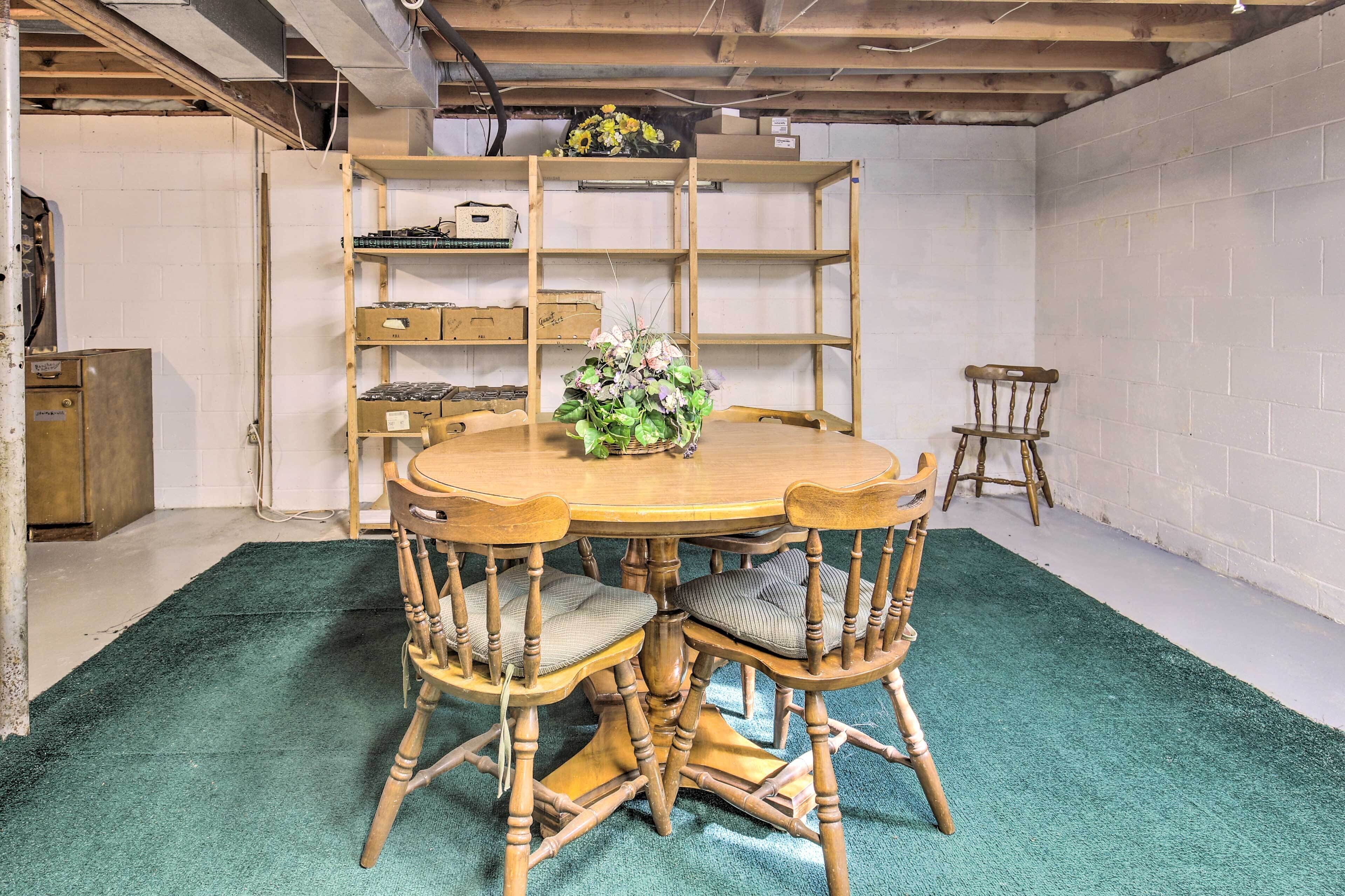 Una mesa de comedor redonda de madera con cuatro sillas, una alfombra verde y una estantería de madera con varios objetos.