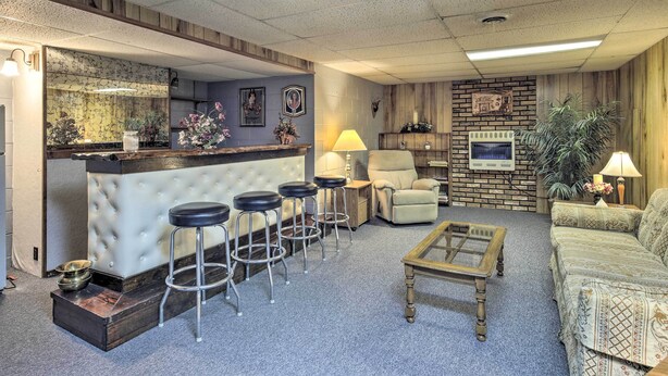 A bar area with stools, a cushioned bar counter, and a seating area with a sofa and armchairs. - Cozy White Pine Home - 10 Mi to Porcupine Mtn (White Pine)