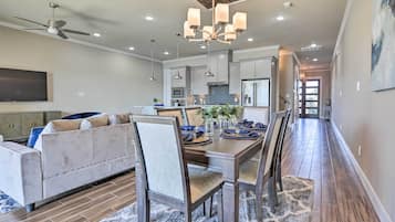 Una cocina moderna con una isla central, un comedor con mesa y sillas de madera, y una sala de estar con sofá y televisor.