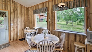 A wooden-paneled room with a round table, white chairs, a vase with flowers, and a television. - Columbia Falls Home 19 Mi to Glacier National Park (Columbia Falls)