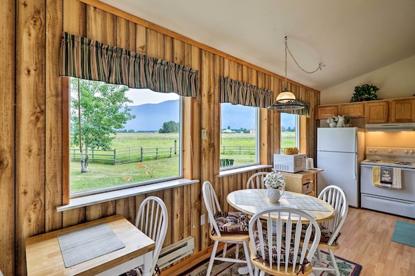 Une cuisine rustique aux murs en bois, une table à manger avec des chaises, et une vue sur un paysage verdoyant par de grandes fenêtres.