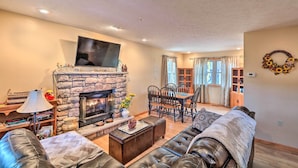 A cozy living room with a stone fireplace, a flat-screen TV, leather sofas, a dining area, and a view of the outside through large windows. - Walk to Pool & Lake: Albrightsville Vacation Home! (Albrightsville)