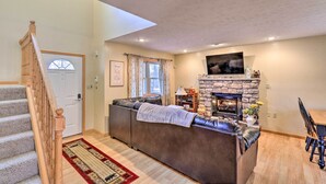 A living room with a stone fireplace, a sofa, a dining table, and a staircase. - Walk to Pool & Lake: Albrightsville Vacation Home! (Albrightsville)