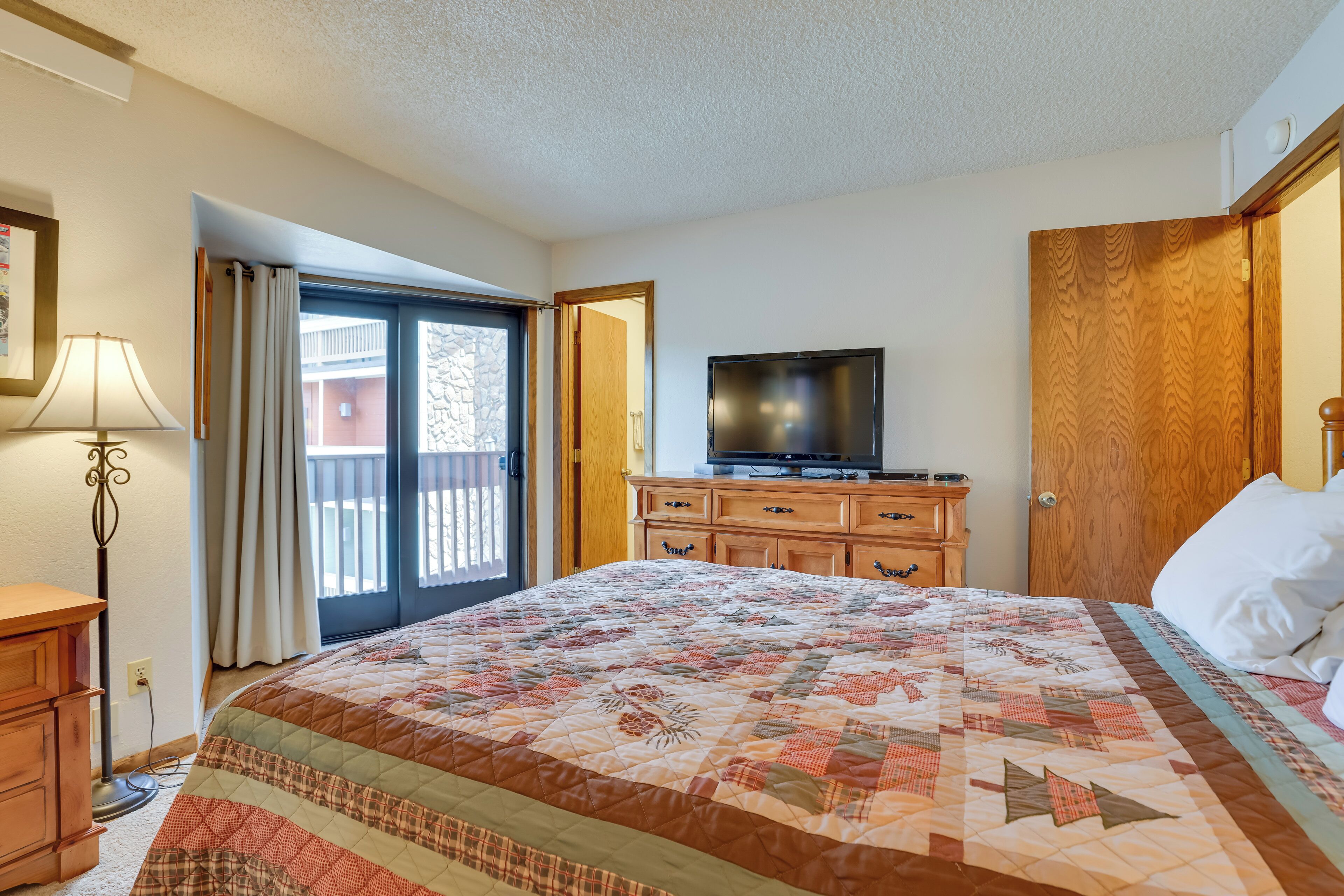 Ein Hotelzimmer mit einem großen Bett, einem Fernseher, einer Holzkommode und einem Balkon mit Vorhängen.