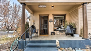 A front porch with a set of steps leading to a door, a bicycle leaning against the railing, and a small table with chairs outside. - Lovely Montrose Home w/ Yard: Walk to Dtwn & Park! (Montrose)
