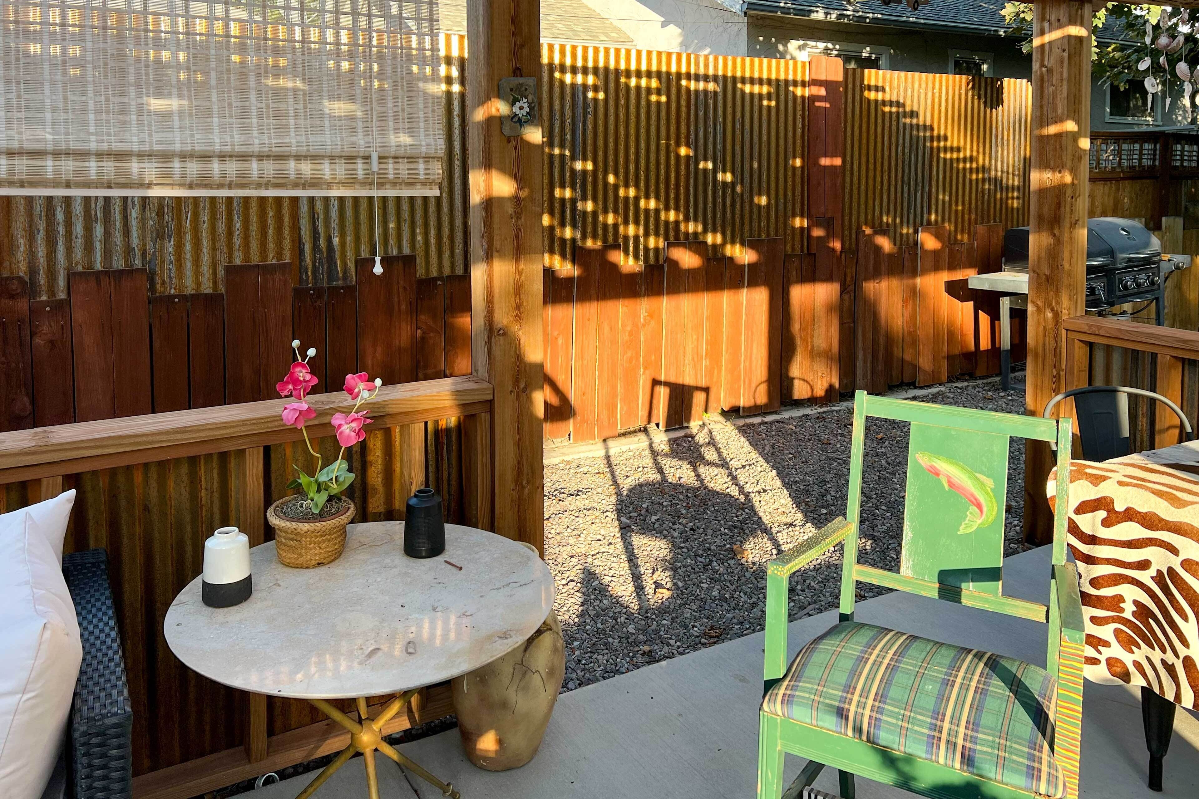 A patio area with a round table, a chair with a green backrest, and a wicker bench.