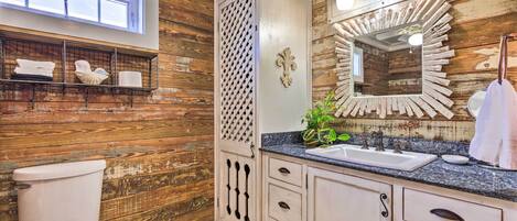 A bathroom with wooden walls, a white toilet, a sink with a mirror, and a shelf with towels.