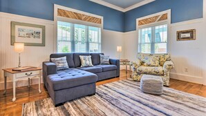 A living room with a grey sectional sofa, a floral armchair, and a striped rug. - Cottage w/ Porch - 3 Min Walk to Bay St Louis (Bay St Louis)