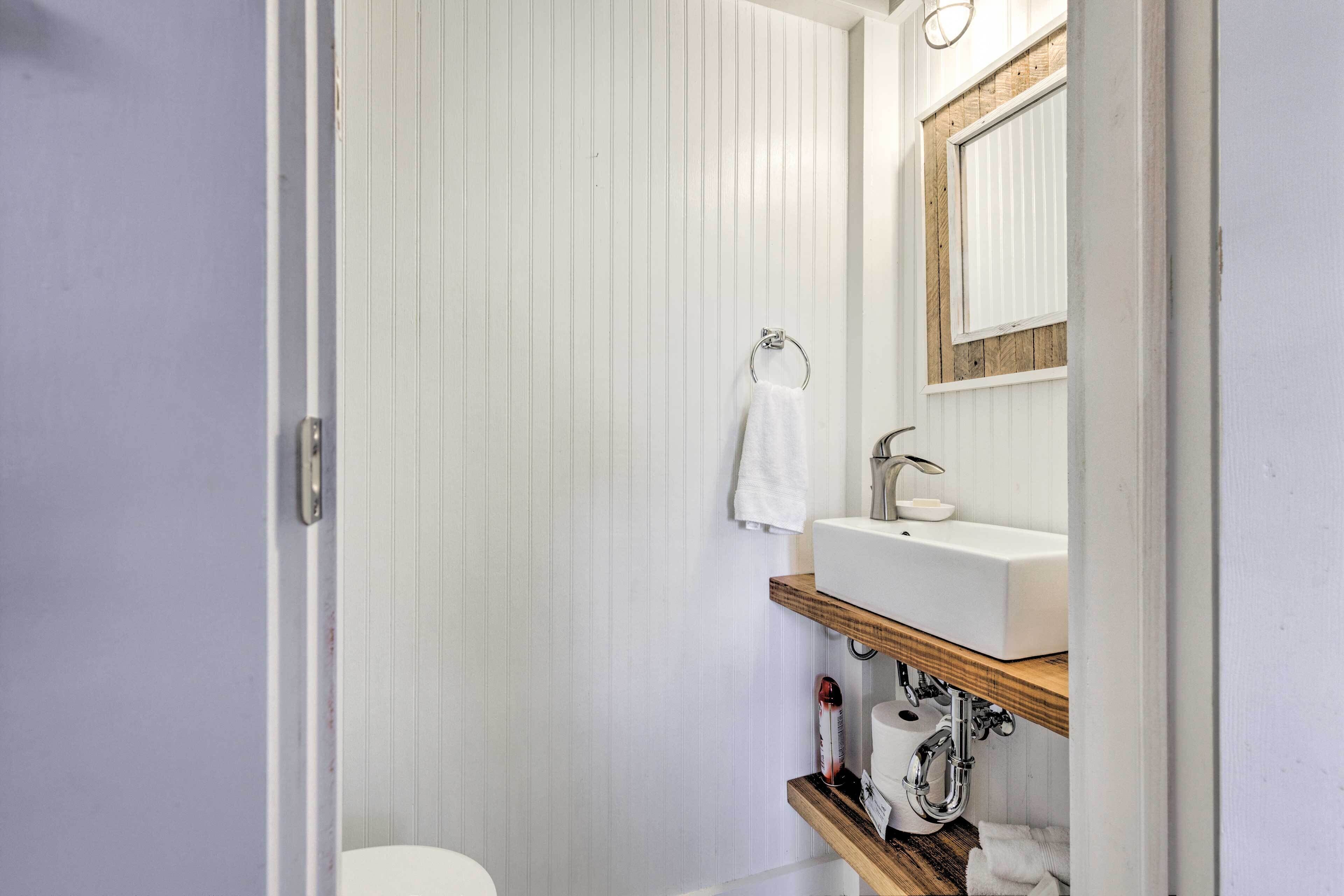 A bathroom with a white toilet, a sink with a wooden shelf, and a mirror above the sink.