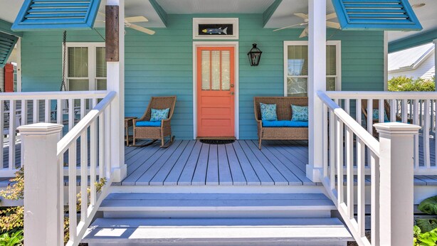 A porch with a red door, two wicker chairs with blue cushions, and a ceiling fan. - Cottage w/ Porch - 3 Min Walk to Bay St Louis (Bay St Louis)