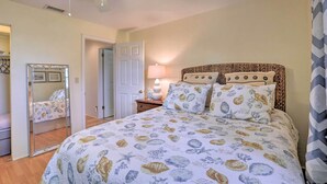 A bedroom with a bed, a nightstand, a lamp, a ceiling fan, a mirror, and a door. - Single-story Home: Walk to Beach, Pier & River (Ormond Beach)