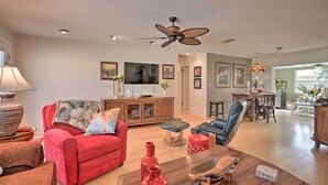 A spacious living room with a red sofa, a wooden coffee table, and a ceiling fan. - Single-story Home: Walk to Beach, Pier & River (Ormond Beach)