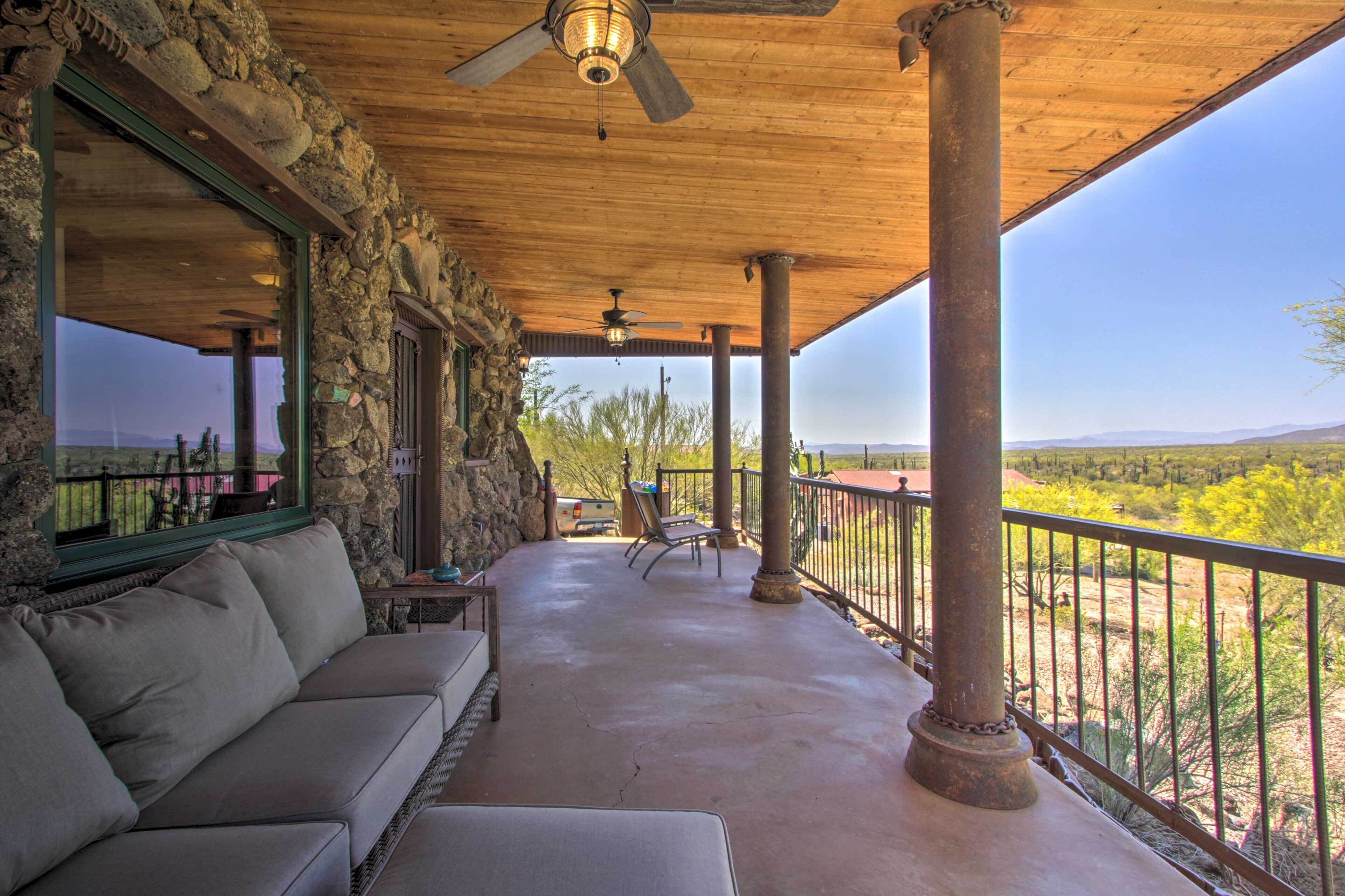 A covered outdoor patio with a stone wall, a sofa, and a view of a desert landscape.