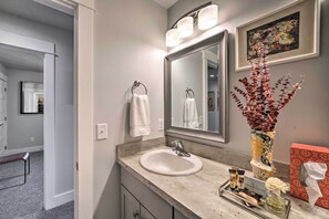A bathroom with a sink, mirror, and towel rack. There is a bench in the hallway and a framed painting on the wall. - Quiet Home by Dtwn Livingston: Hike, Fish & Ski! (Livingston)