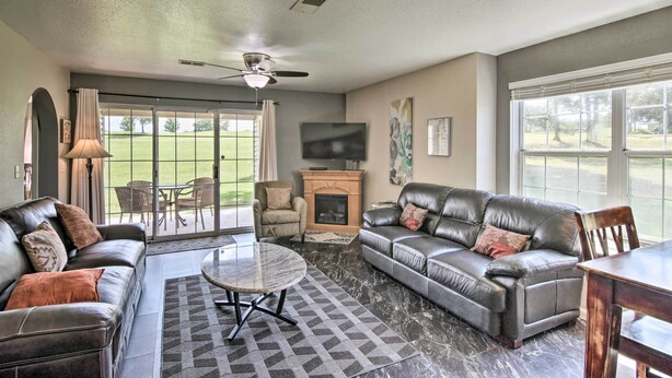 A spacious living room with leather sofas, a fireplace, a flat-screen TV, and a patio area with a view of a golf course. - Holiday Hills Resort Condo w/ Hot Tub Access (Branson)