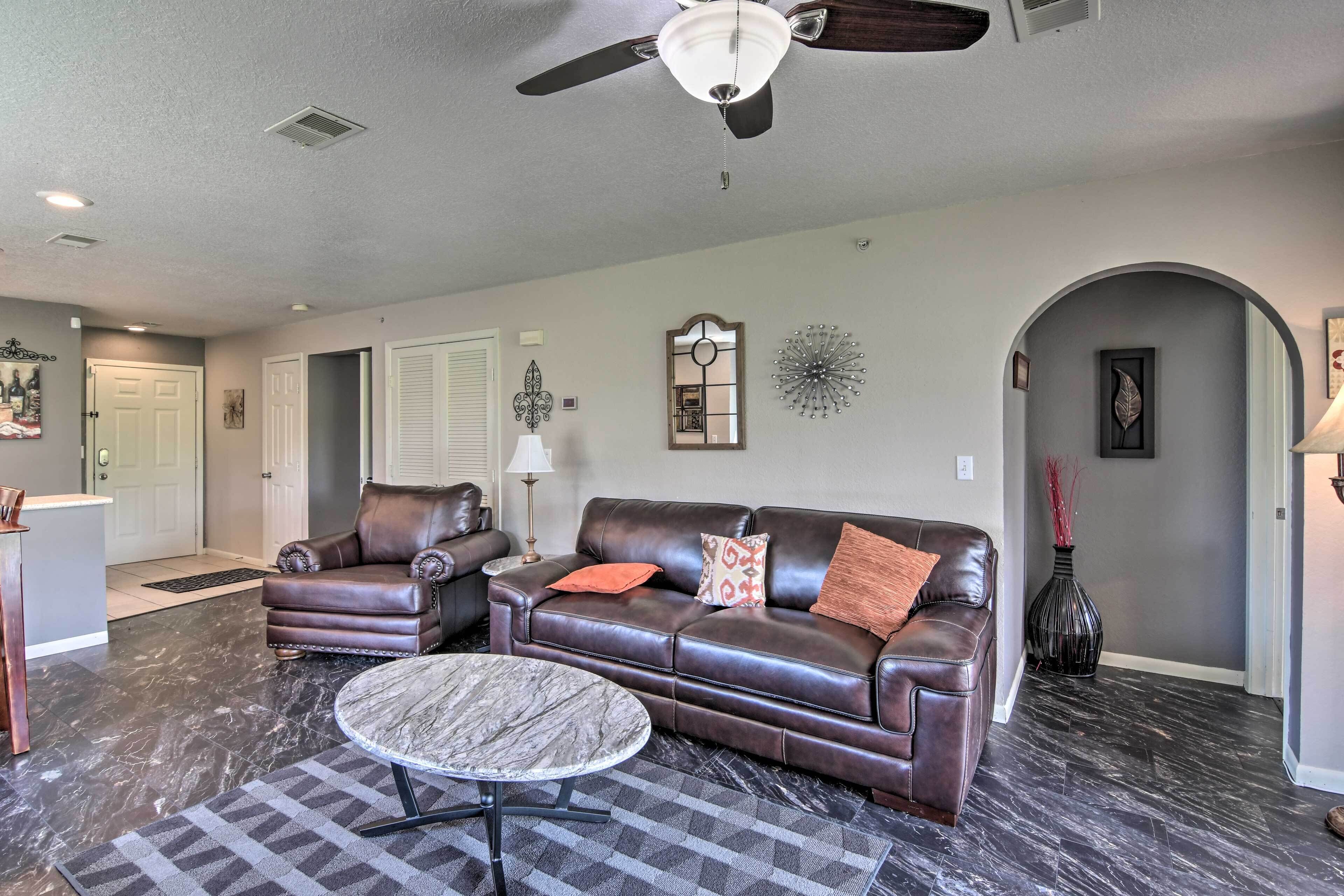 A living room with a dark brown leather sofa, a matching armchair, and a marble coffee table.