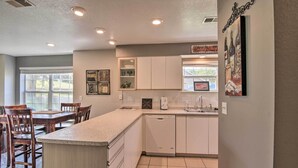 A kitchen with white cabinets, a granite countertop, a dishwasher, and a dining area with wooden chairs and a table. - Holiday Hills Resort Condo w/ Hot Tub Access (Branson)
