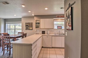 A kitchen with white cabinets, a granite countertop, a dishwasher, and a dining area with wooden chairs and a table. - Holiday Hills Resort Condo w/ Hot Tub Access (Branson)
