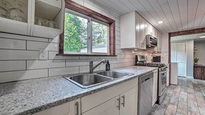 A kitchen with a double sink, granite countertop, white cabinetry, and a window with a view of trees.