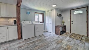 A laundry room with two front-loading washers and dryers, a wooden beam, a small table with a potted plant, and a door with a window.