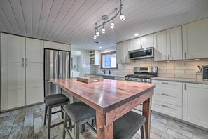 Une cuisine moderne avec des meubles blancs, des appareils en acier inoxydable et un îlot central en bois doté de tabourets de bar.