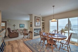 A cozy living room with a fireplace, a dining area with wooden chairs, and a large window overlooking a snowy landscape.