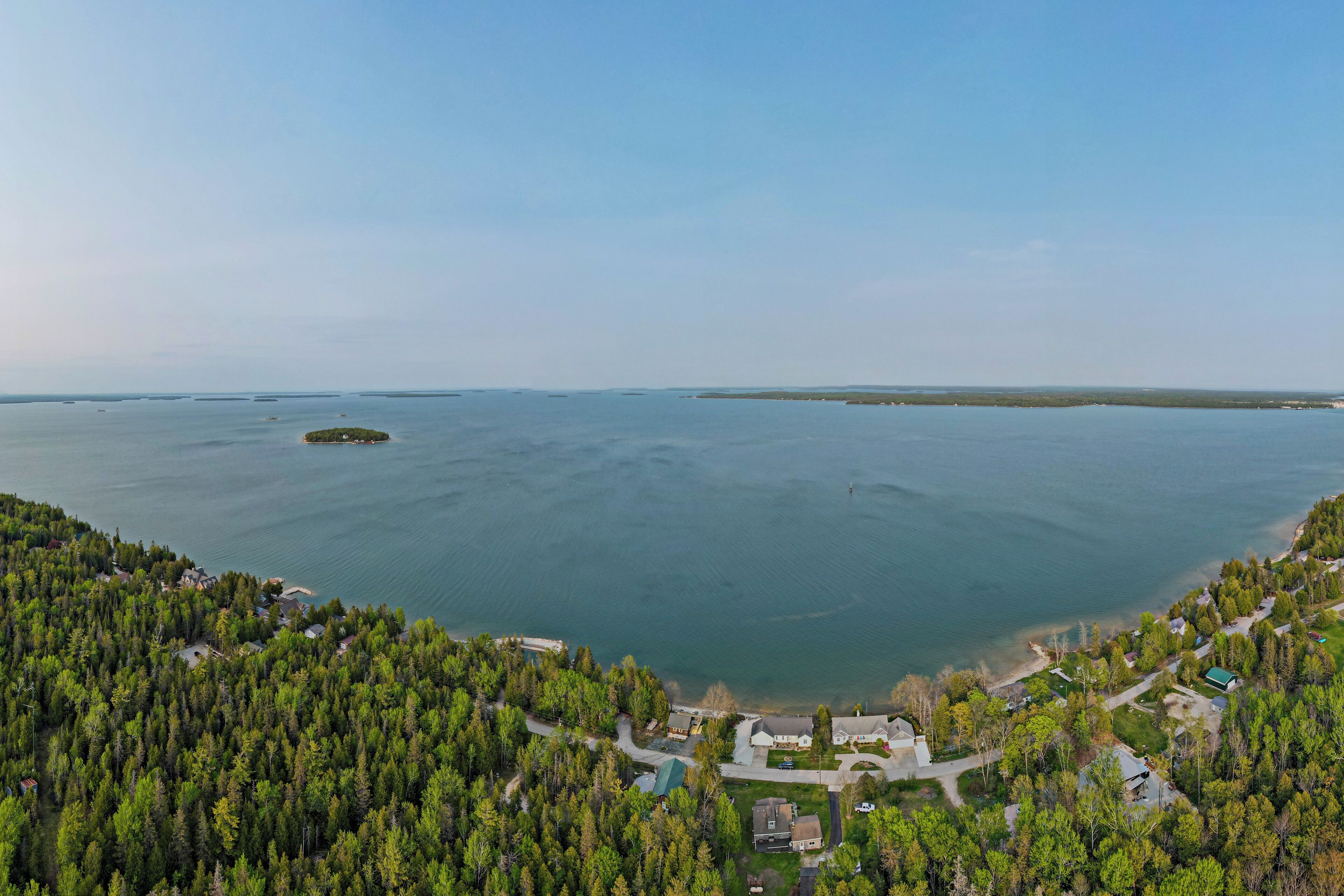 An aerial view of a coastal area with dense forest, a small island, and a clear view of the water.