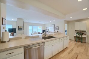 A modern kitchen with a dishwasher, a sink, and a dining area with a view. - Lakefront De Tour Village Home w/ Deck & Fire Pit! (De Tour Village)