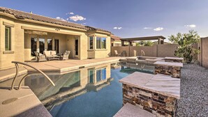 A swimming pool with a stone deck and lounge chairs, surrounded by a house with a tiled roof and a covered patio area. - Updated Goodyear Escape: Remote-work Friendly (Goodyear)
