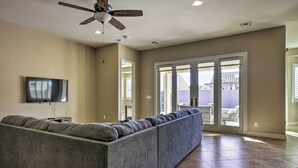 A living room with a sectional sofa, a ceiling fan, a flat-screen TV, and a sliding glass door leading to an outdoor patio. - Updated Goodyear Escape: Remote-work Friendly (Goodyear)