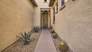 A narrow pathway leading to a wooden door, flanked by cacti and small plants, with textured walls and a small window above. - Updated Goodyear Escape: Remote-work Friendly (Goodyear)