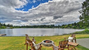 Zona de estar al aire libre junto al lago con sillas tipo Adirondack y un brasero.