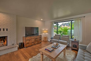 Een woonkamer met een open haard, een televisie, een bank en uitzicht op de omgeving.