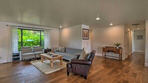 Amplia sala de estar con piso de madera, un sofá gris, un sillón de cuero oscuro y una mesa de centro de madera.