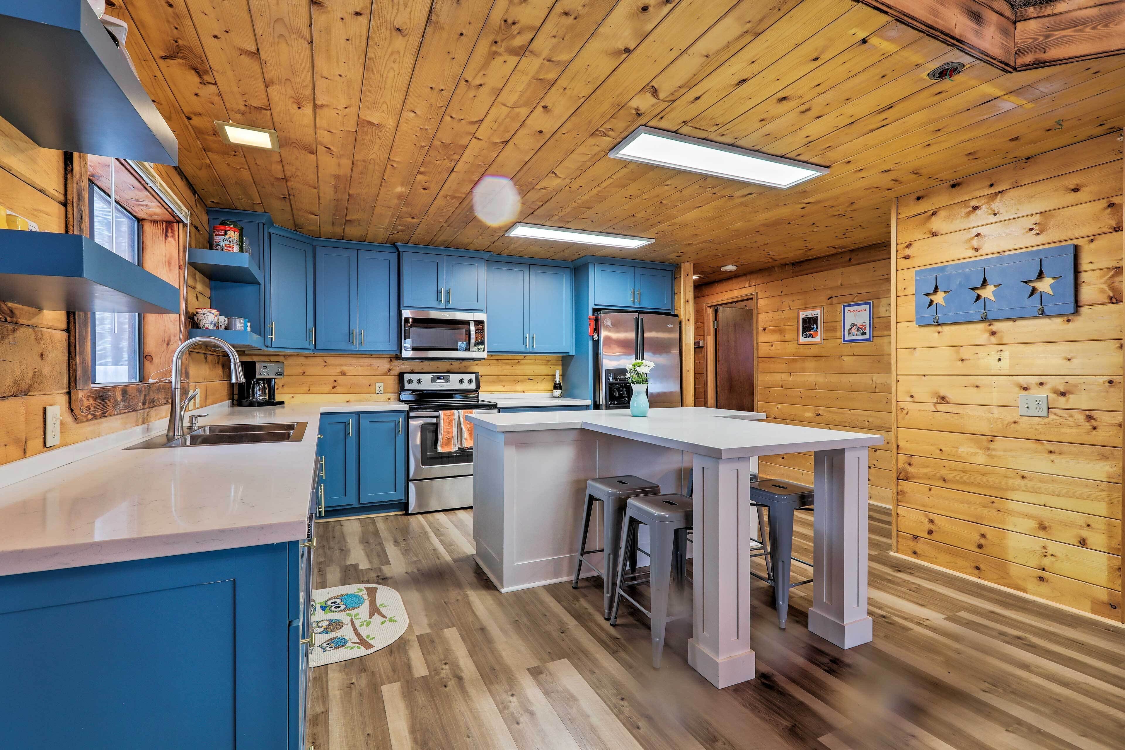 A modern kitchen with blue cabinets, stainless steel appliances, and a central island with stools.