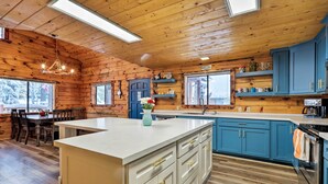 A cabin-style kitchen with wooden walls, a central island, blue cabinets, and a dining area with a table and chairs. - Furnished Deck: Cabin in Coconino National Forest (Munds Park)