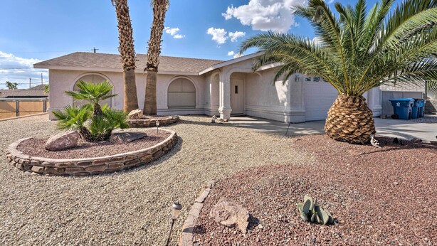 A single-story house with a stucco exterior, a garage, and a landscaped front yard with palm trees and a small garden. - Temp-controlled Pool: Lake Havasu Escape, Mtn View (Lake Havasu City)