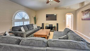 A spacious living room with a ceiling fan, a large window with blinds, a flat-screen TV, and a fireplace. - Temp-controlled Pool: Lake Havasu Escape, Mtn View (Lake Havasu City)
