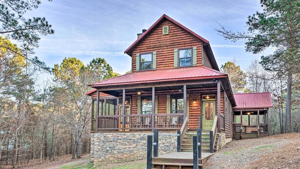 A log cabin with a stone foundation, a red roof, and a porch with wooden railings. - Broken Bow Cabin w/ Deck, Hot Tub & Fire Pit! (Broken Bow)