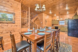 A wooden interior with a dining table set for six, a staircase, and a kitchen area.